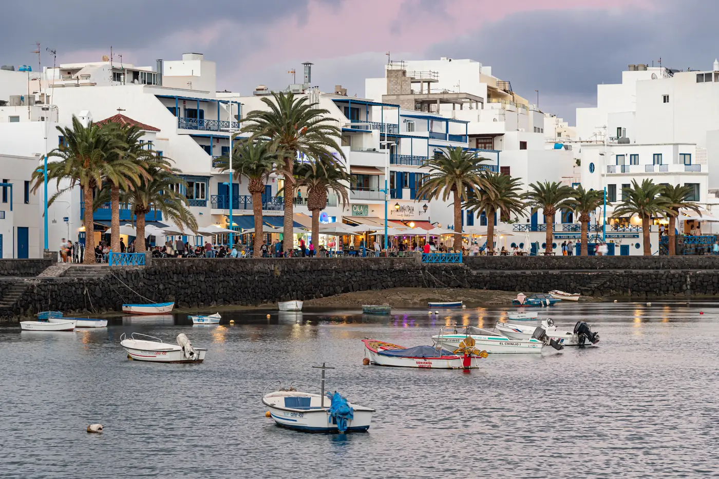Small boats on the Charco de San Ginés lagoon in Arrecife, below white waterfront houses and palms.