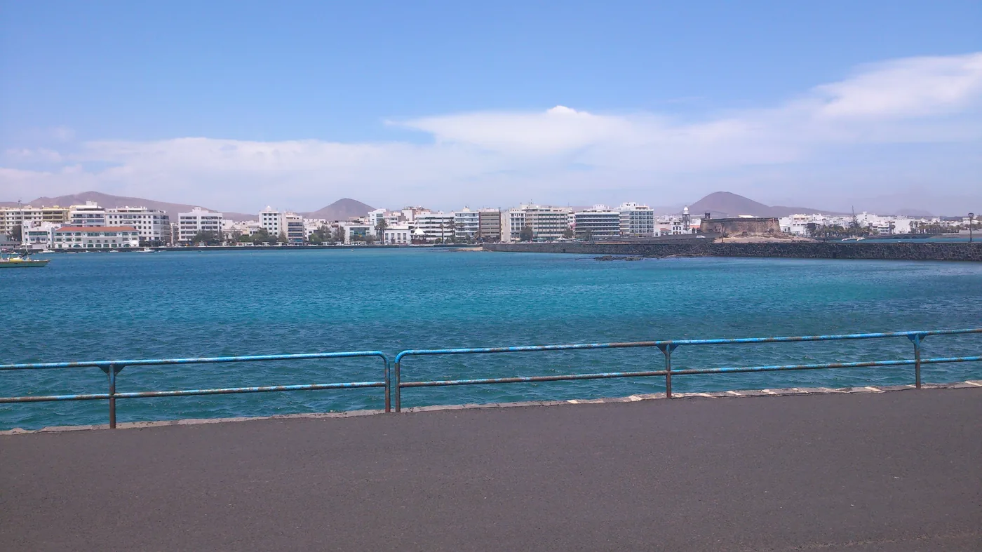 Arrecife waterfront seen across bright blue water, with the city and hills beyond.