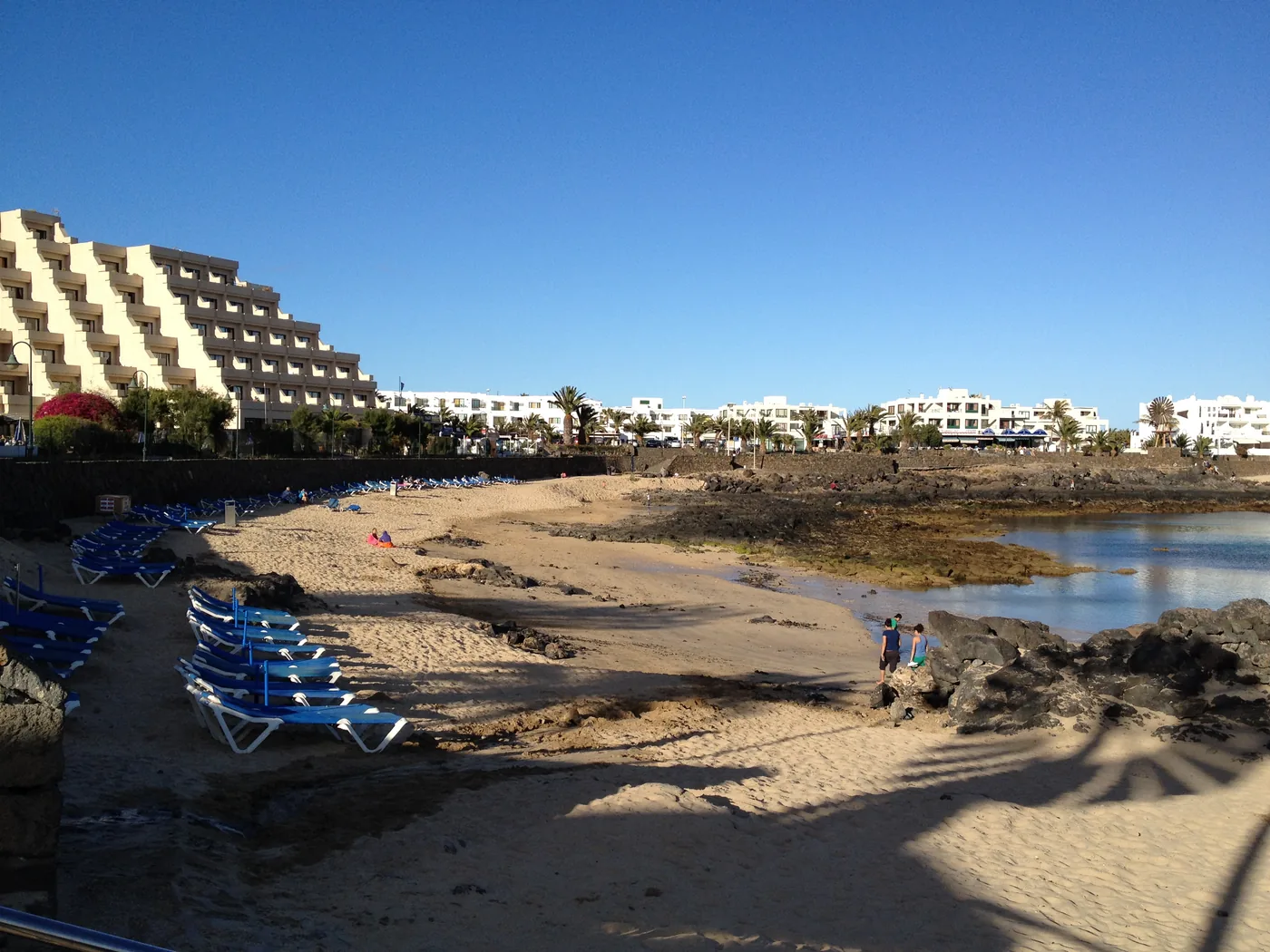 The small sandy bay of El Jablillo in Costa Teguise, with sunbeds and a stepped hotel behind.