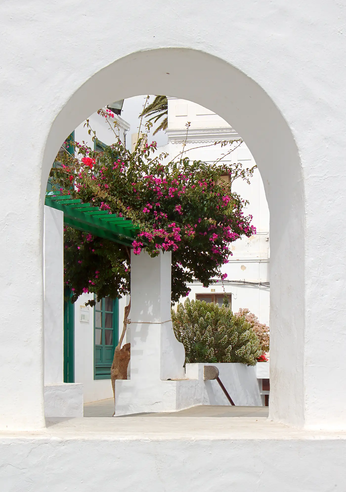 A whitewashed arch in Haría framing bougainvillea and a white house.