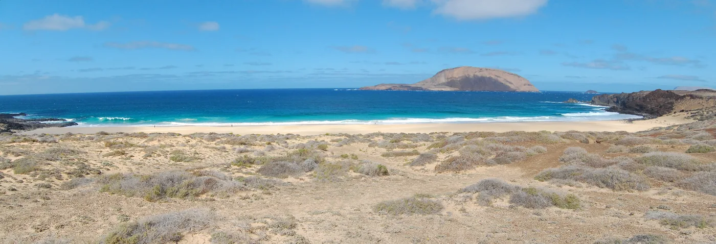 The long pale beach of Playa de las Conchas on La Graciosa, with an islet offshore.