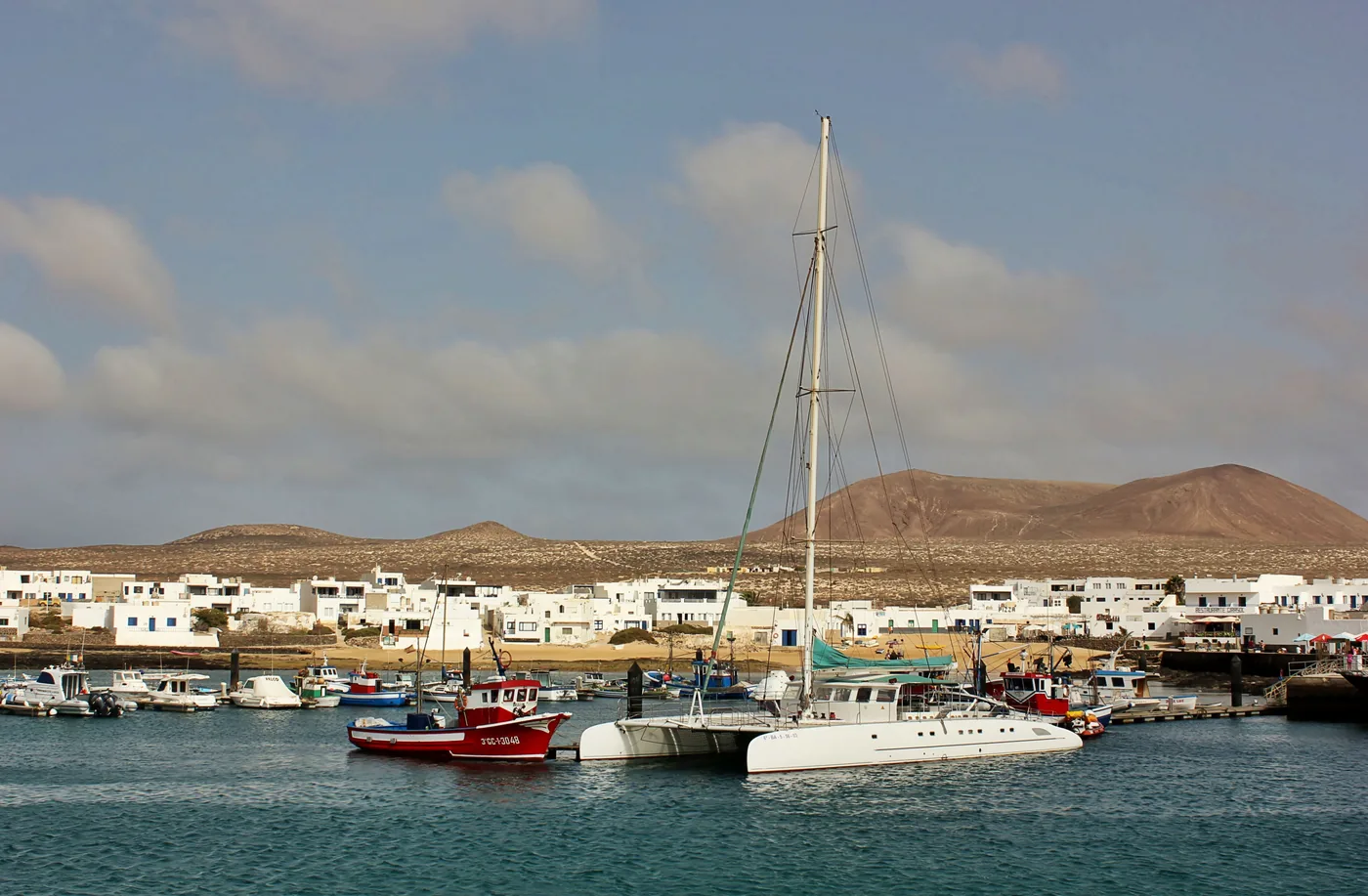 Boats in Caleta de Sebo harbour with La Graciosa's white village and volcanic hills beyond.