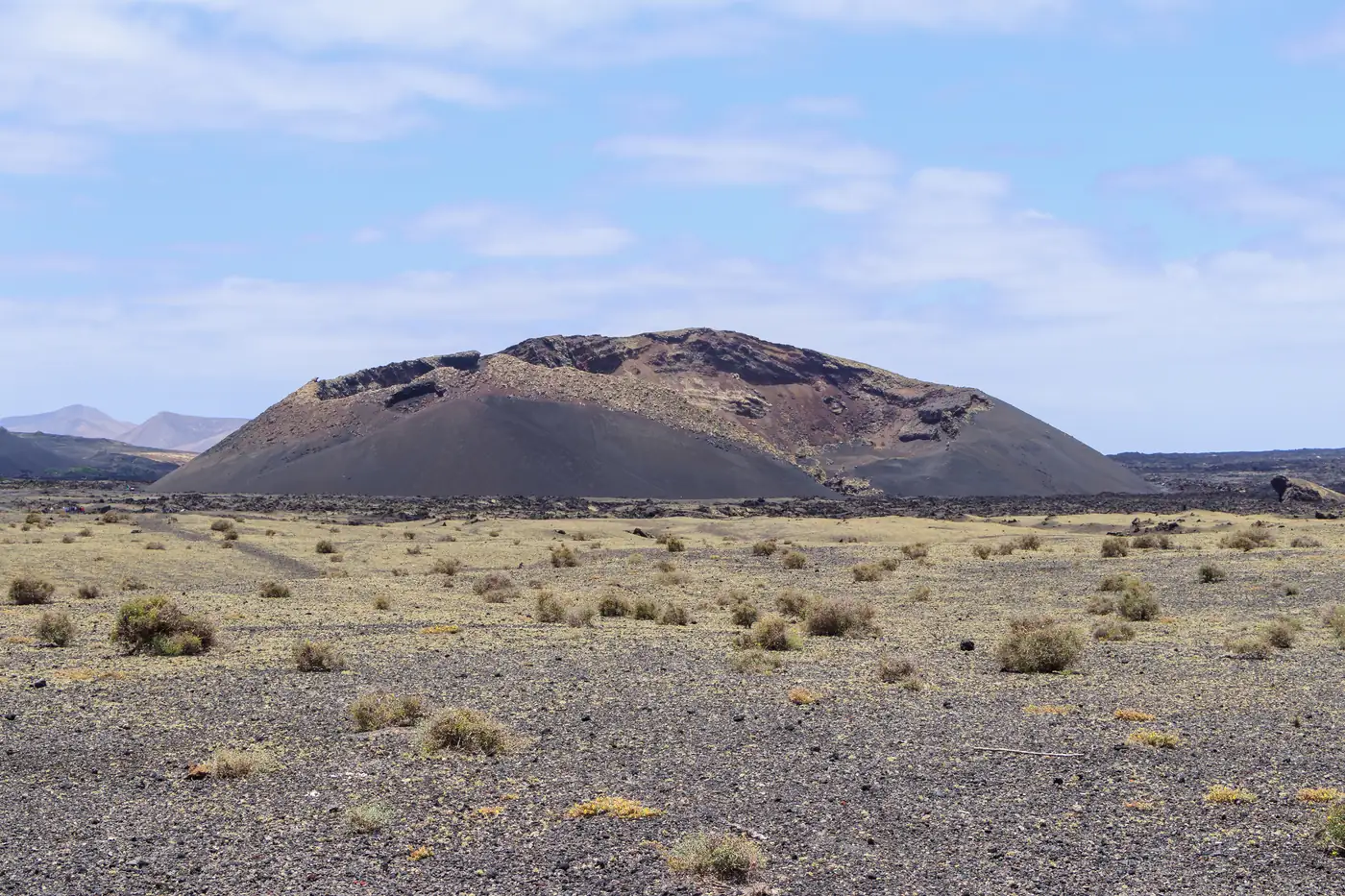 The dark cone of Volcán del Cuervo above a plain of lava gravel and low scrub.
