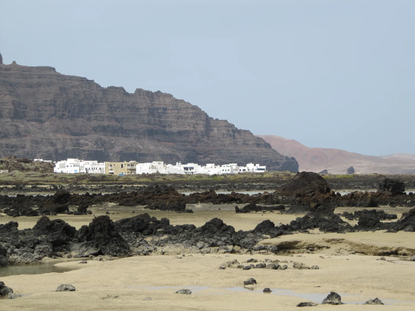 Órzola's white houses seen across a shore of sand and black lava, below the Famara cliffs.