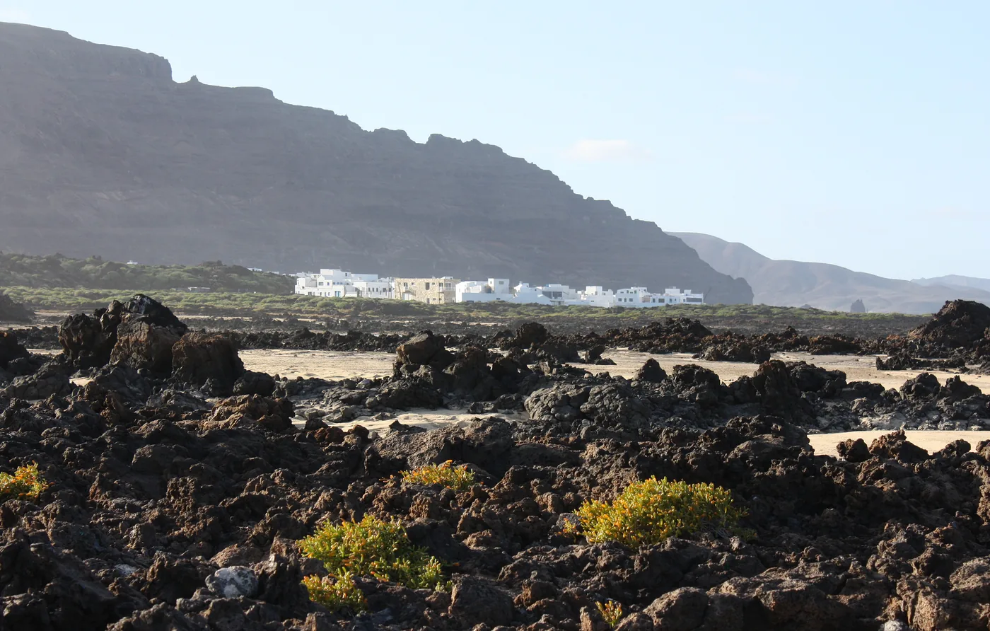 Órzola's white village beyond a rugged field of black volcanic rock on Lanzarote's north coast.