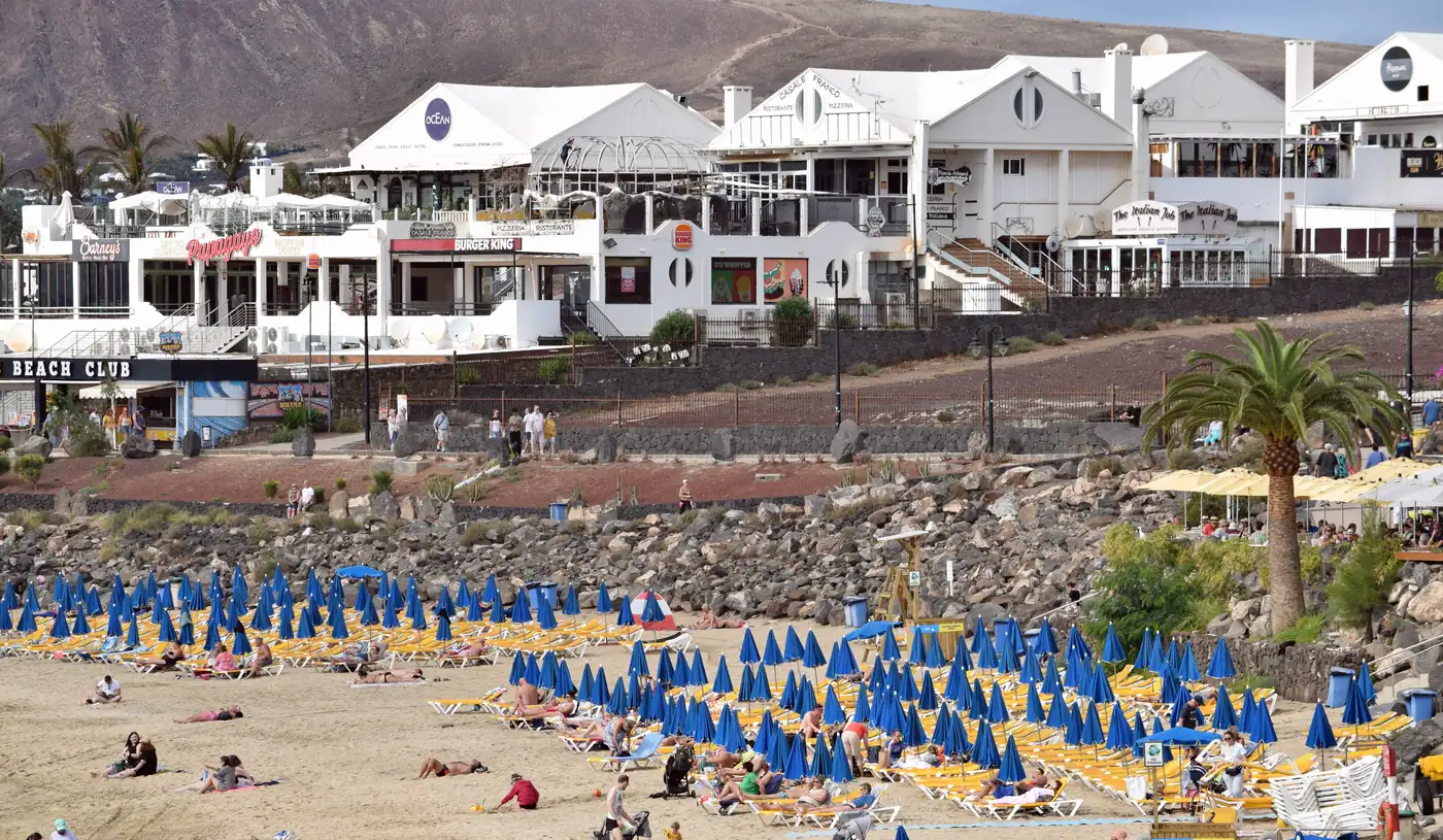 Playa Dorada busy with blue sunshades below white seafront buildings in Playa Blanca.