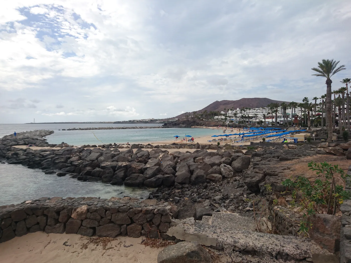 Playa Flamingo's sheltered beach behind a stone breakwater in Playa Blanca, with palms and hills beyond.