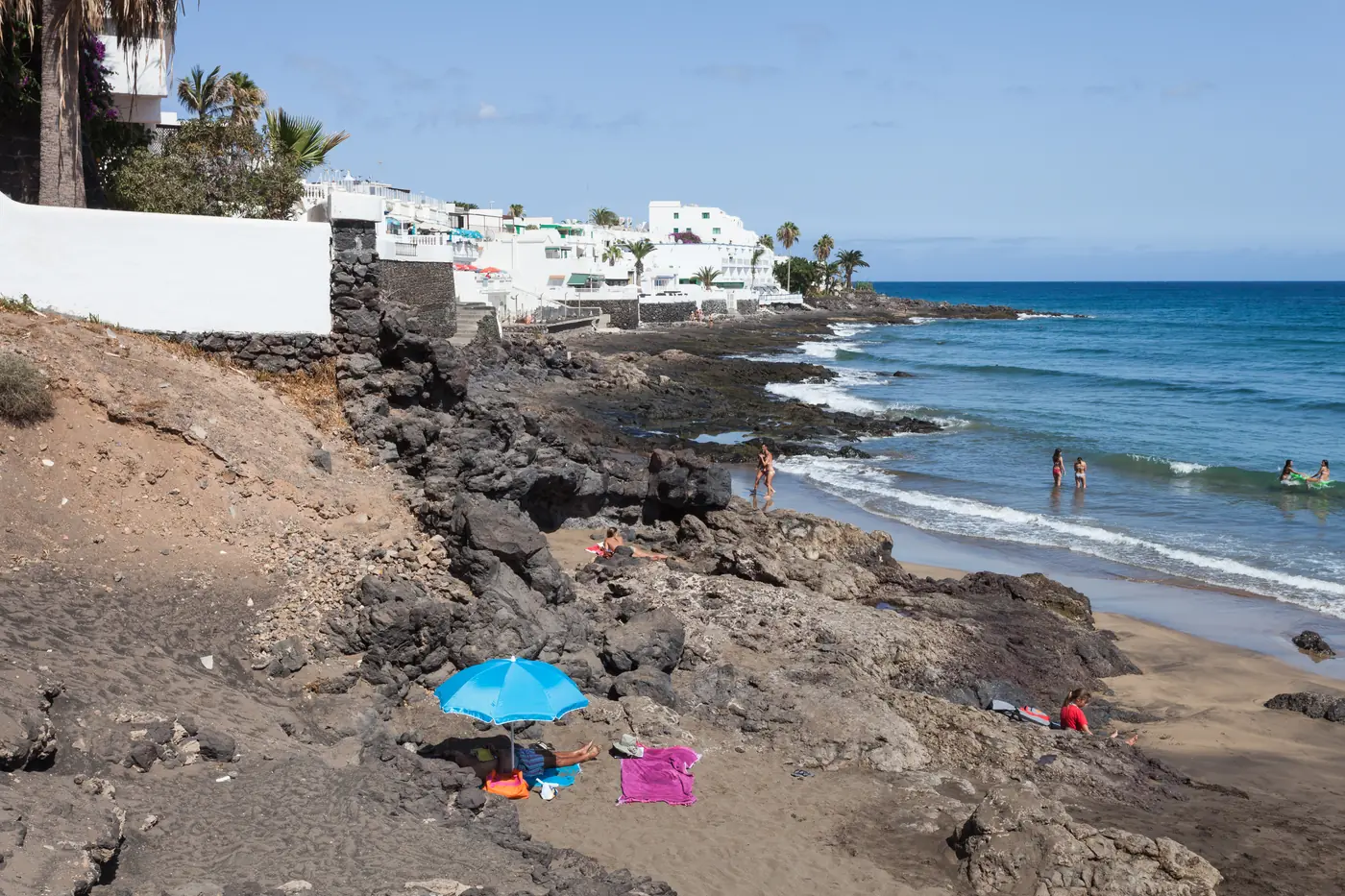 A golden beach below dark rocks and white buildings in Puerto del Carmen.