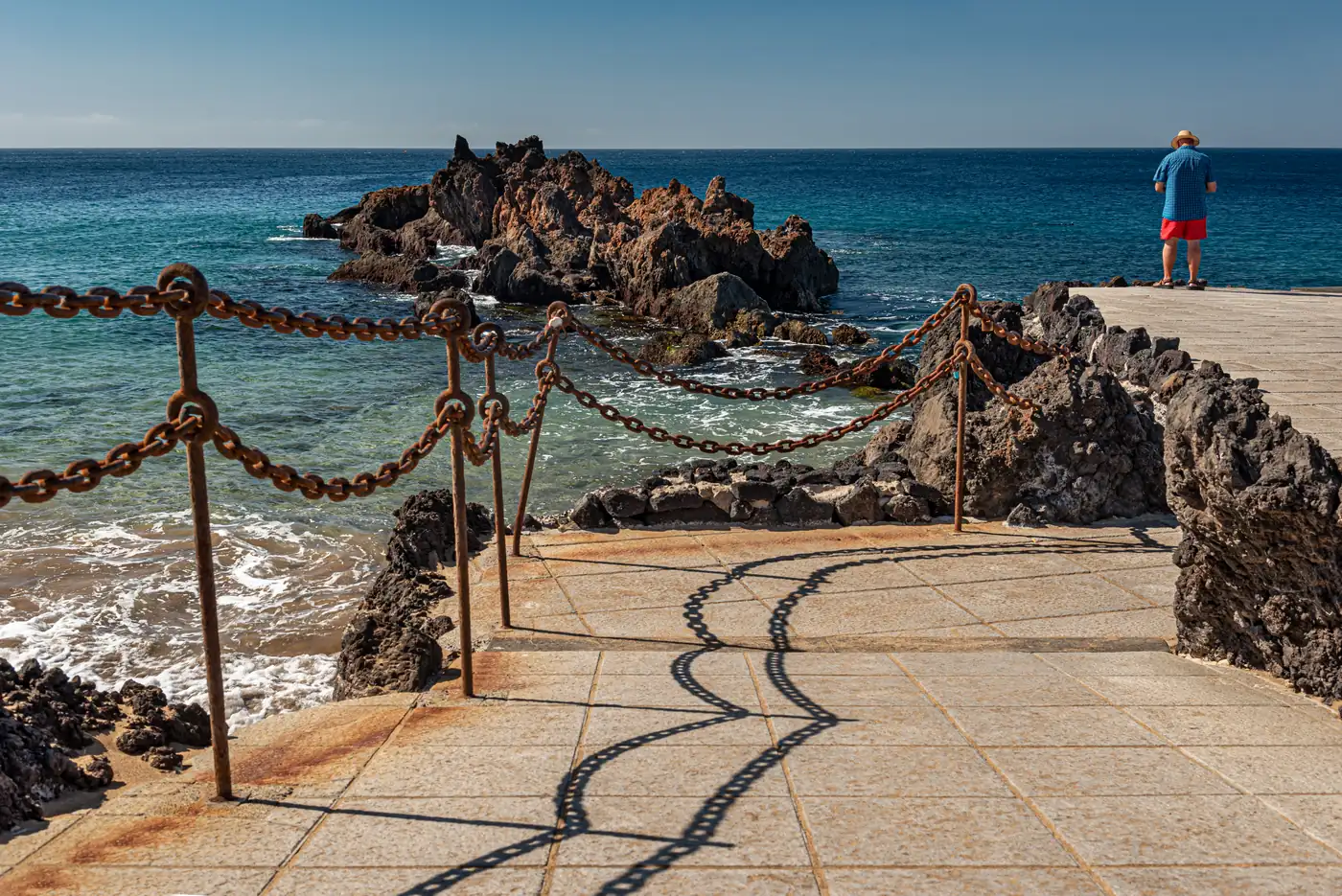 A paved viewpoint with chain railings on dark rocks above the sea by Playa Chica, Puerto del Carmen.