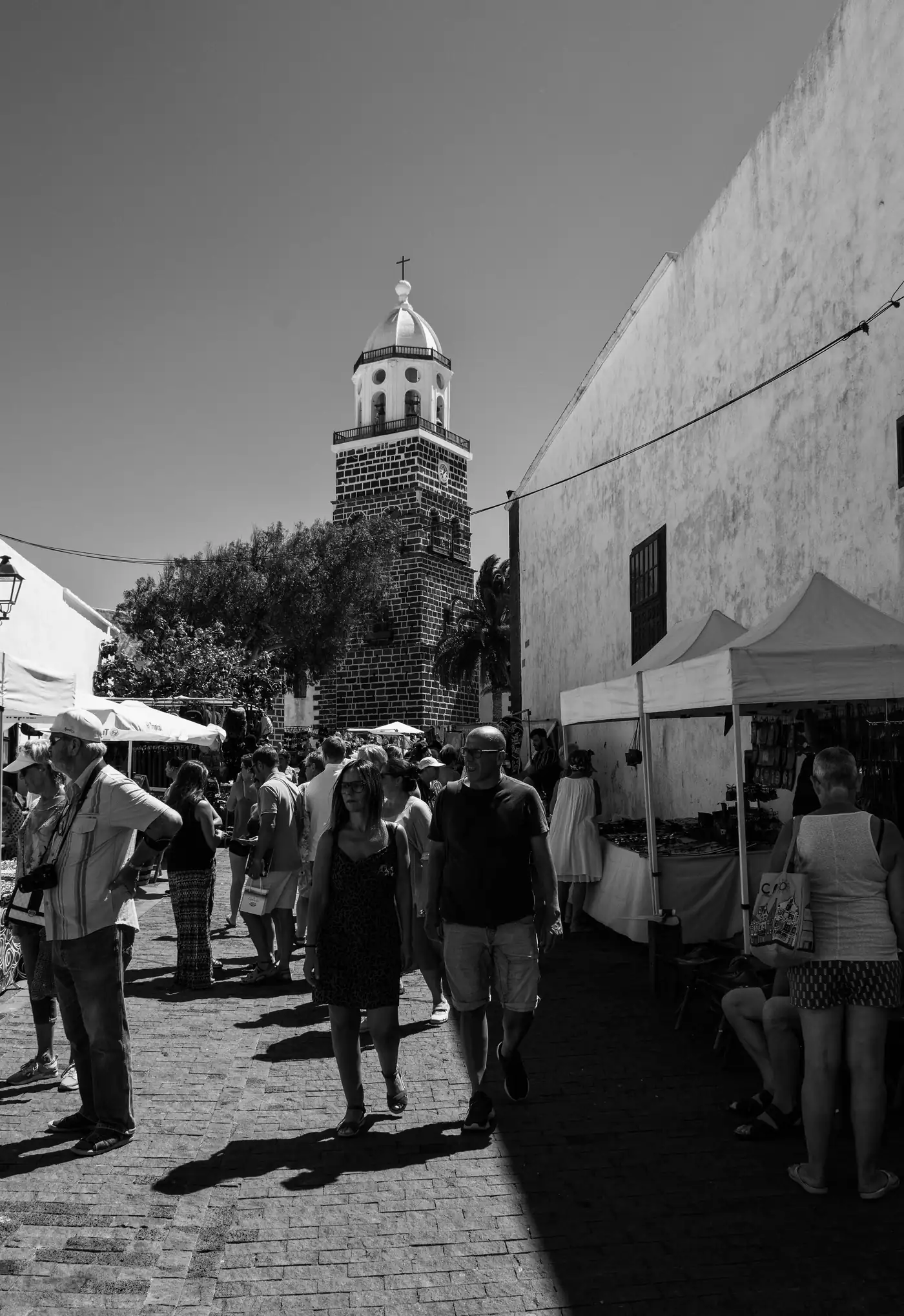 Black-and-white view of market stalls in a Teguise street, with the church tower behind.