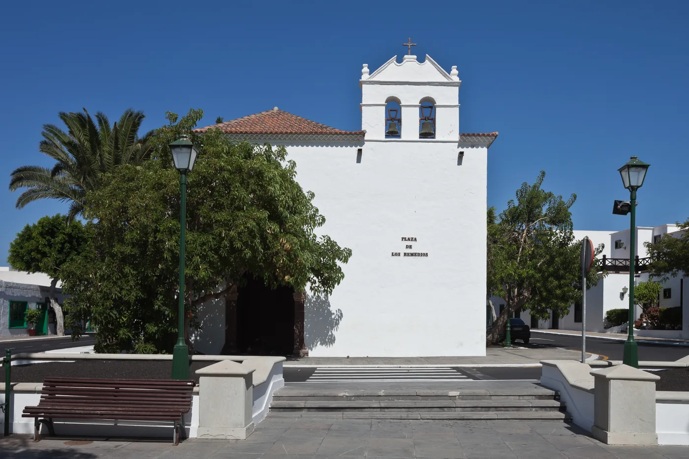 The white church of Nuestra Señora de los Remedios on its square in Yaiza, under a blue sky.
