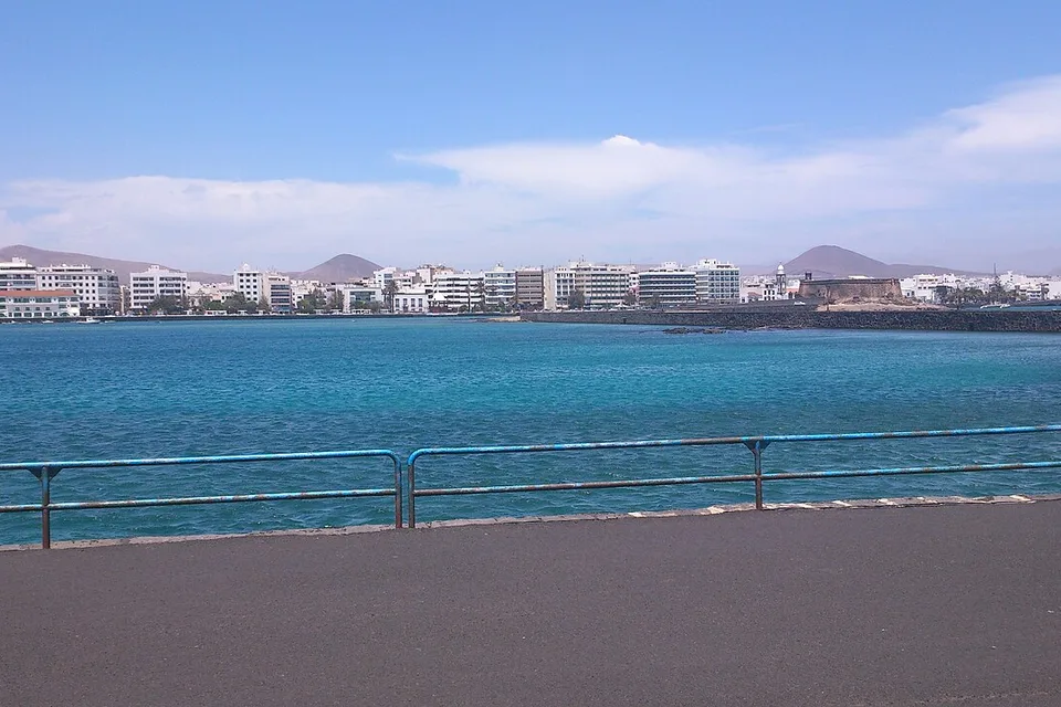 Arrecife waterfront seen across bright blue water, with the city and hills beyond.