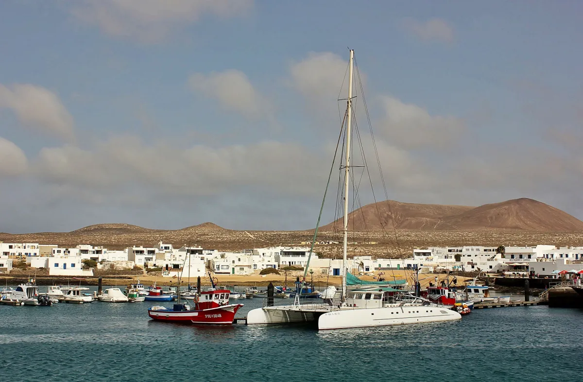 Boats in Caleta de Sebo harbour with La Graciosa's white village and volcanic hills beyond.