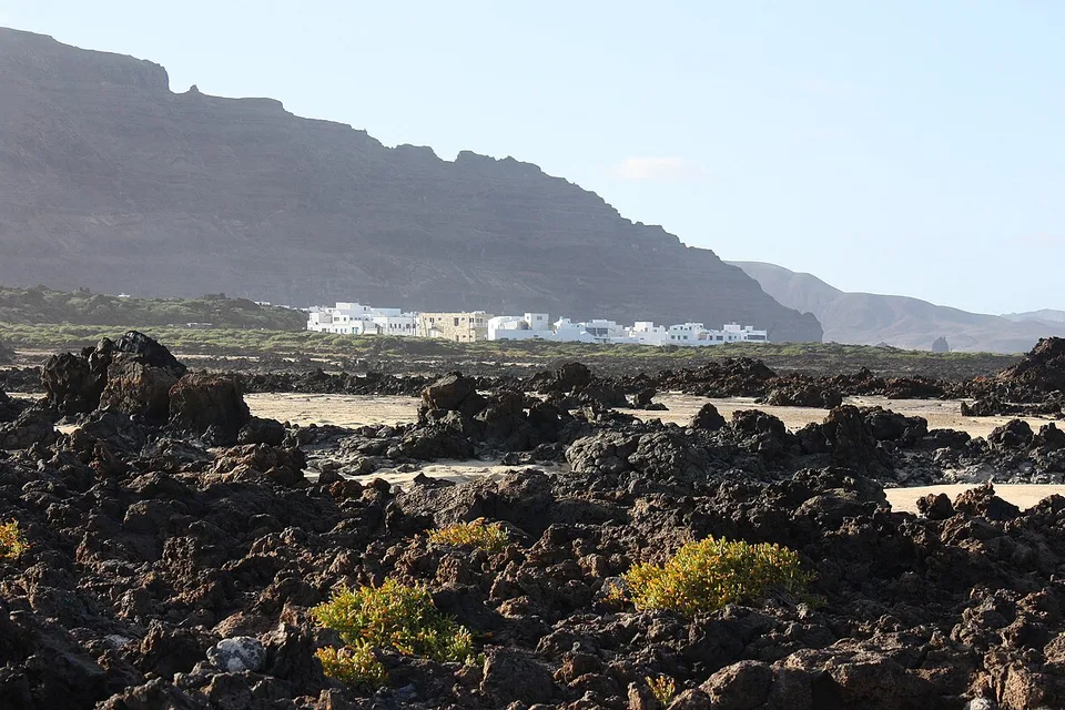 Órzola's white village beyond a rugged field of black volcanic rock on Lanzarote's north coast.
