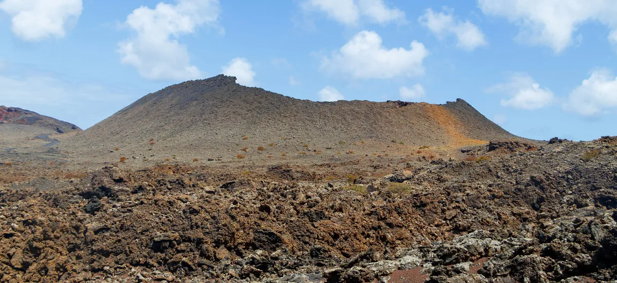 Layered lava fields and a volcanic crater on the controlled Volcano Route in Timanfaya National Park.